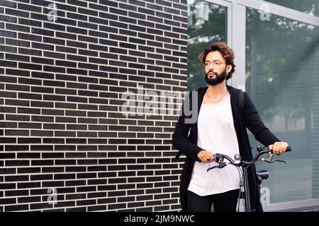 giovane uomo caucasico che cammina con la sua moto, concetto di stile di vita urbano e mobilità sostenibile, spazio di copia per il testo Foto Stock