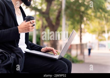 uomo alla moda irriconoscibile che lavora con un computer portatile bevendo caffè all'aperto in città, concetto di tecnologia e stile di vita urbano, spazio copia Foto Stock