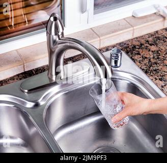 Bicchiere da bere che viene riempito con acqua di rubinetto da cucina Foto Stock