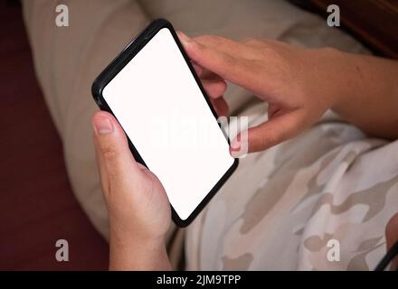 Primo piano di un uomo che utilizza un telefono cellulare con uno schermo vuoto a casa. Foto Stock
