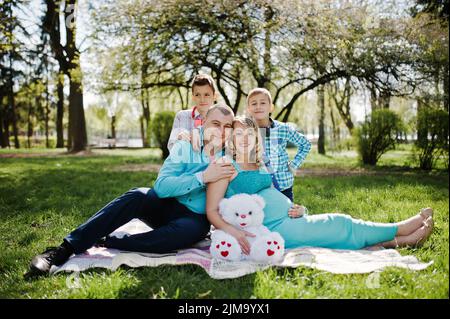 Gravidanza felice coppia con due figli e avvolgente seduta su plaid sfondo natura a molla Foto Stock