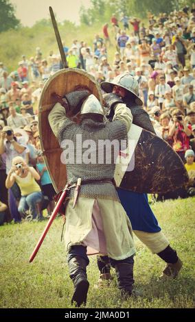 Samara, Russia, la festa della ricostruzione storica antica Russia età 11-13 - 11 agosto 2013: Battaglia di due guerrieri in caschi e catena di posta, spade e scudi al festival della ricostruzione storica sul campo con il pubblico Foto Stock