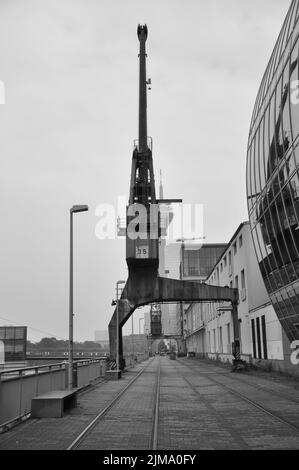 Un'immagine verticale in scala di grigi di una vecchia gru da carico nel Media Harbor di Dusseldorf, Germania. Foto Stock