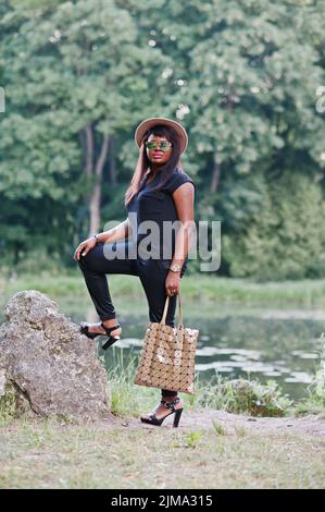 African American plump donna al cappello e occhiali da sole con il sacchetto in mano Foto Stock