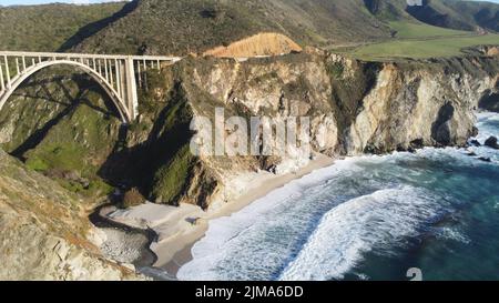 Una vista panoramica del Bixby Creek Bridge sopra le onde dell'oceano che si infrangono contro una costa rocciosa della California Foto Stock