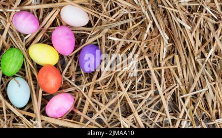 Uova colorate per le vacanze pasquali che formano il bordo sinistro su paglia naturale e legno Foto Stock