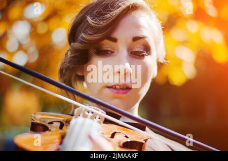 Ritratto di ragazza intelligente con violino sulle mani per esterno in cappotto marrone in autunno. Foto Stock