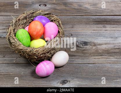 Vista frontale ravvicinata delle uova di Pasqua colorate nel nido d'uccello su tavole rustiche di legno. Foto Stock