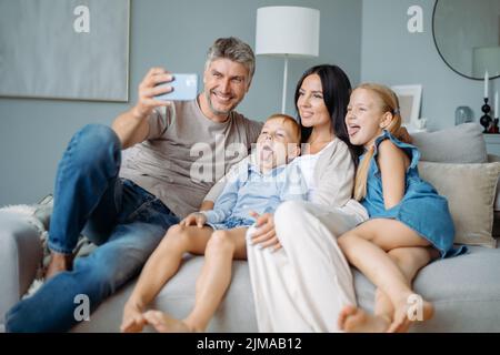 famiglia felice con i bambini che si divertono a scattare selfie seduti sul divano. Foto Stock