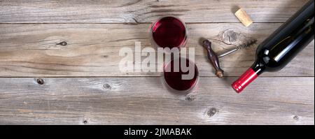 Bottiglia di vino rosso non aperta con cavatappi vecchi e bicchieri pieni su tavole rustiche di legno Foto Stock