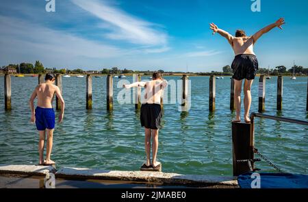 Tre ragazzi adolescenti si prepararono a tuffarsi in mare ad alta marea a Bosham, West Sussex, Regno Unito. Foto Stock