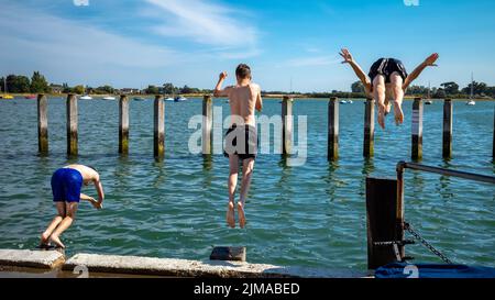 Tre ragazzi adolescenti si prepararono a tuffarsi in mare ad alta marea a Bosham, West Sussex, Regno Unito. Foto Stock