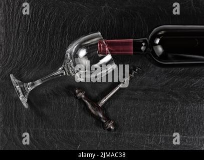 Vista dall'alto del cavatappi d'annata con bottiglia di vino rosso e bicchiere da bere su sfondo di ardesia nera Foto Stock