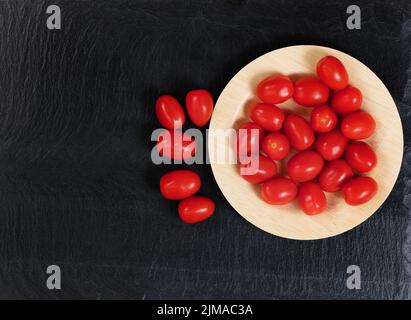 Vista dall'alto di pomodori ciliegini biologici in un piatto di bambù su sfondo ardesia Foto Stock