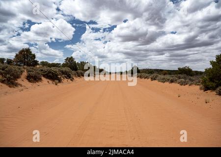 La strada ghiaiosa di sabbia rossa nello Utah conduce sempre dritto. Foto Stock