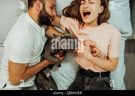 Il Bulldog francese Bite Woman's Finger mentre si stese sul letto con l'uomo Foto Stock