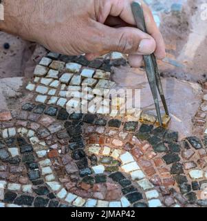 Vista ravvicinata di un archeologo che restaura un pavimento a mosaico presso l'antica Messene (Ithomi), la Messinia, il Peloponneso meridionale, la Grecia Foto Stock