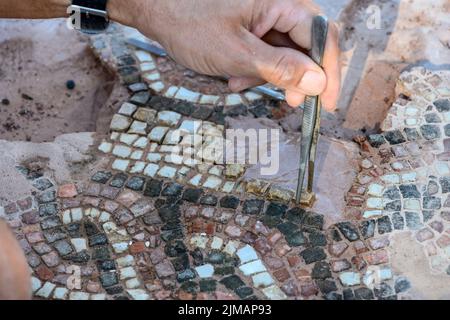 Vista ravvicinata di un archeologo che restaura un pavimento a mosaico presso l'antica Messene (Ithomi), la Messinia, il Peloponneso meridionale, la Grecia Foto Stock