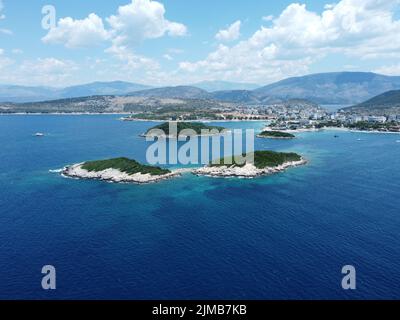 Isole tropicali Ksamil nel Mediterraneo, Riviera albanese vicino alla spiaggia con città e montagne Foto Stock