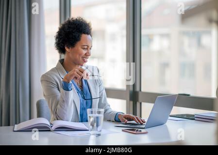 Donna d'affari sorridente con occhiali che utilizzano un computer portatile. Le donne che indossano i formali sono sedute alla scrivania. Lavora in ufficio aziendale. Foto Stock