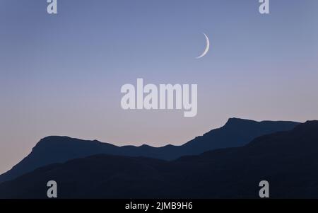 Una luna crescente in un cielo azzurro-arancione pallido mentre il tramonto si dissolve in un'ora blu con le montagne (Sgiath Chuil) in primo piano Foto Stock