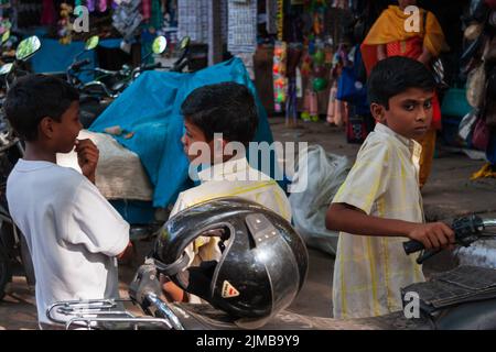 Tre ragazzi giocano con moto parcheggiate nell'affollato centro di Chennai Foto Stock