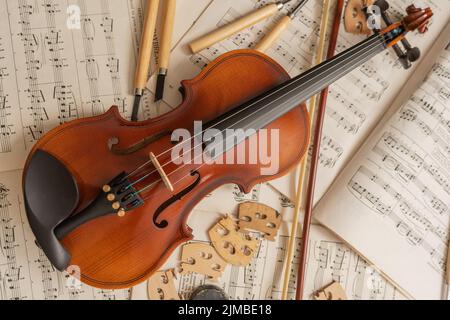 Vista dall'alto di un violino sulla parte superiore di fogli musicali in un laboratorio con strumenti e pezzi Foto Stock