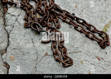 Un primo piano di una catena metallica arrugginita che giace su un pavimento in cemento Foto Stock