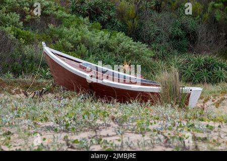 Vecchio pescatore abbandonato barca adagiata sulle dune di sabbia circondata da piante e alberi a Las Flores spiaggia, Maldonado, Uruguay Foto Stock