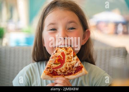 Una giovane ragazza con le trecce sta mangiando un pezzo di pizza. Foto di alta qualità Foto Stock