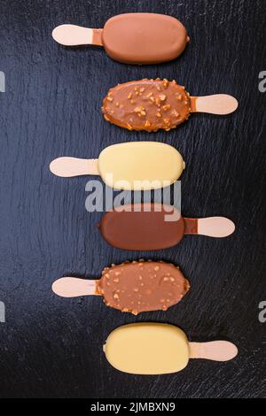 Gelato sul bastone ricoperto di cioccolato su ardesia nera Foto Stock