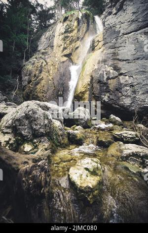 Bella cascata con alberi e foglie rosse, delle rocce e delle pietre nella foresta di autunno. Foto Stock