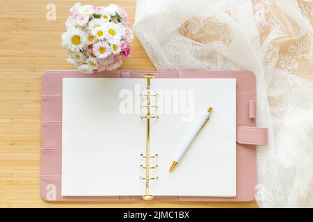 Piatto, vista dall'alto di un pianificatore color rosa pastello, bouquet di fiori e cancelleria su una scrivania in legno. Foto Stock