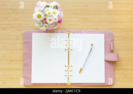 Piatto, vista dall'alto di una pianta rosa pastello, bouquet di fiori e cancelleria su una superficie di legno. Foto Stock