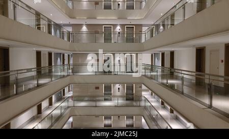 Un interno di un hotel con due ascensori e balconi di vetro in tonalità pastello Foto Stock