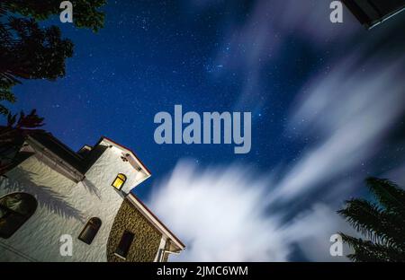 Un'inquadratura a basso angolo di una lunga esposizione delle nuvole in una notte stellata con un edificio in primo piano Foto Stock