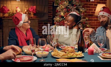 Donne allegre e diverse che parlano al tavolo della cena di Natale mentre si gusta il tradizionale cibo cucinato in casa. I membri della famiglia multietnica felici ridono a cuore mentre festeggiano la festa dell'inandiere. Foto Stock