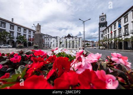 Fiori rossi e rosa con 'Portas da Cidade', la città simbolo di Ponta Delgada sullo sfondo. Isola di São Miguel nelle Azzorre, Portogallo. Foto Stock
