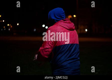 Ragazzo al buio nel cofano. Persona sconosciuta sulla strada. L'uomo in giacca rossa nasconde il suo volto. Abbigliamento di stile moderno. Foto Stock