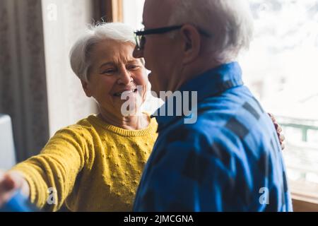 Felice romantica coppia sposata ridendo e ballando in soggiorno, tenendo le mani, avendo divertimento in pensione durante le vacanze invernali. Foto di alta qualità Foto Stock