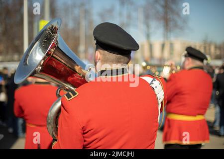 Il trombettista suona in orchestra. Musicista con strumento musicale eolico. Vestiti rossi. Esecuzione della melodia sulla tromba. Foto Stock