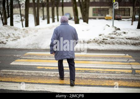 La donna attraversa la strada sulla zebra. Il pensionato in Russia cammina per la strada. L'uomo cammina sull'attraversamento pedonale. Riprese dal retro. Foto Stock