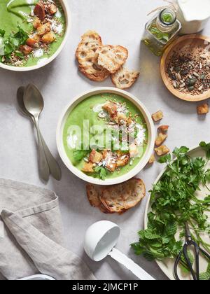 Vista dall'alto della gustosa zuppa di panna verde con prezzemolo sormontato da crostini posti sul tavolo con verdure in cucina leggera Foto Stock