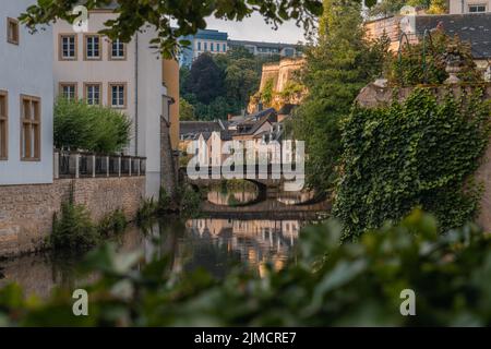 Scenario tranquillo di un piccolo ponte ad arco in pietra sul fiume tranquillo che scorre tra vecchi edifici residenziali in una giornata di sole a Lussemburgo Foto Stock