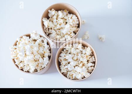 Vista dall'alto di secchi in cartone riempiti di gustosi popcorn preparati per guardare film e serviti su sfondo bianco in una sala luminosa Foto Stock