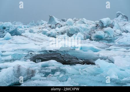 Scenario pittoresco di terreno ghiacciato con un massiccio ghiacciaio e ghiacci contro il cielo nuvoloso grigio in Islanda Foto Stock