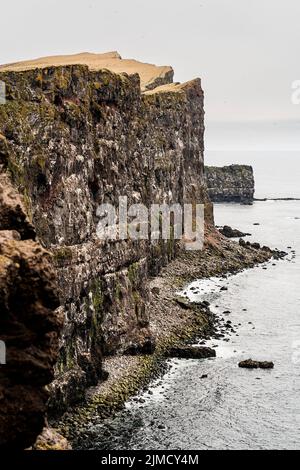 Ruvida scogliera rocciosa con superficie irregolare situata sulla riva vicino al mare sotto il cielo sovrastato nella zona costiera nella natura dell'Islanda Foto Stock