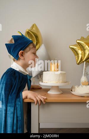 Ragazzo biondo con vista laterale che soffia le candele durante una festa di compleanno Foto Stock