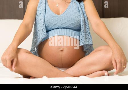 Gravidanza, riposo, persone e concetto di aspettativa - felice donna incinta seduta sul letto e toccare h Foto Stock