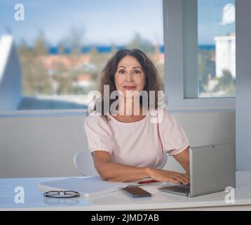 Ritratto interno di una bella donna sorridente anziana che lavora a. casa Foto Stock